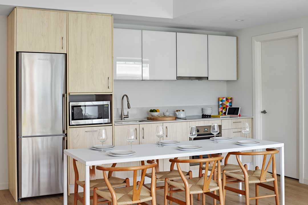 Open floor plan kitchen with white counters, wooden cabinets, refrigerator, microwave, flat-top stove, oven.