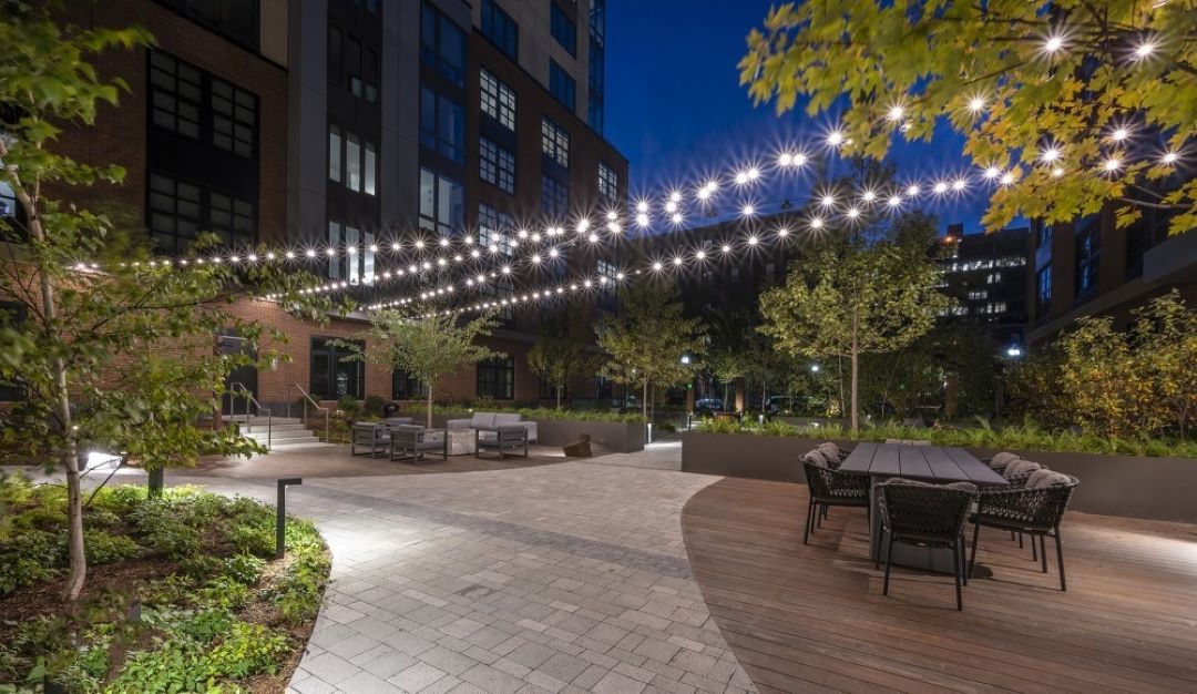 Nighttime view of landscaped patio with walkways, public seating areas, ambient lighting, and skyline views