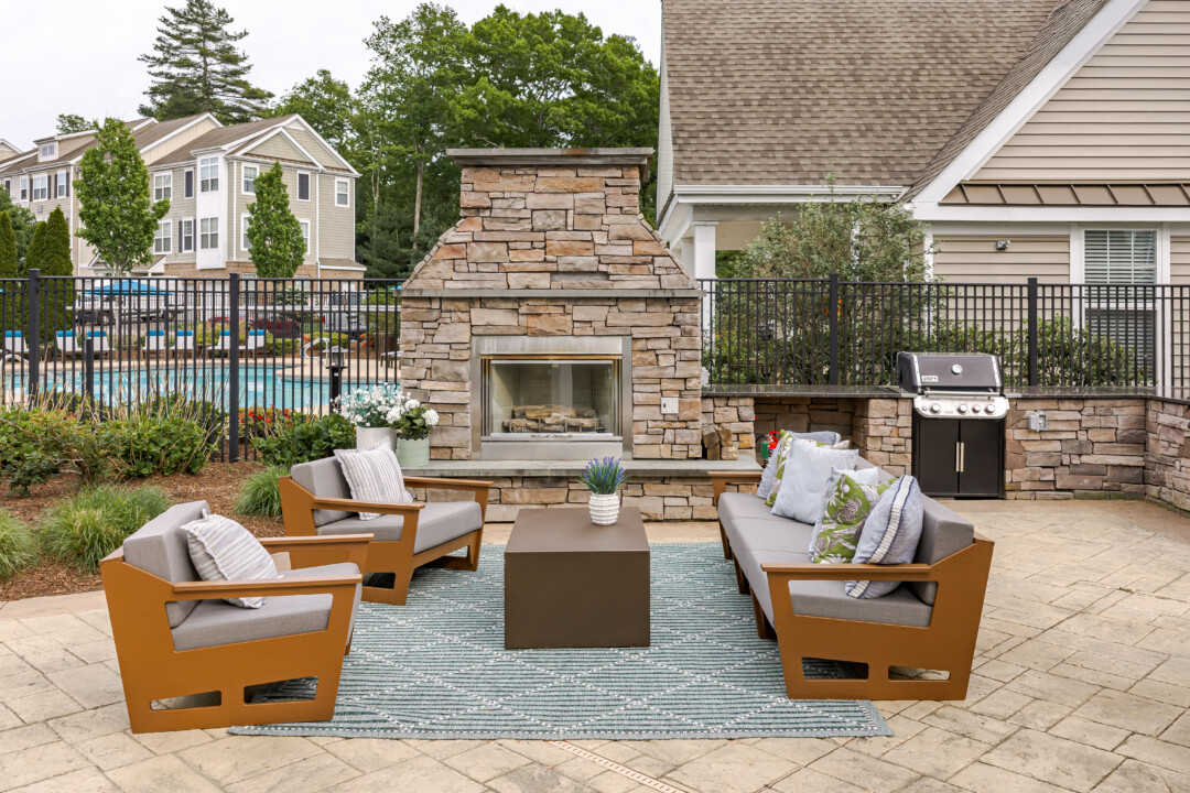 Outdoor gathering space featuring a stone fireplace, grilling stations, comfortable seating, and poolside views.