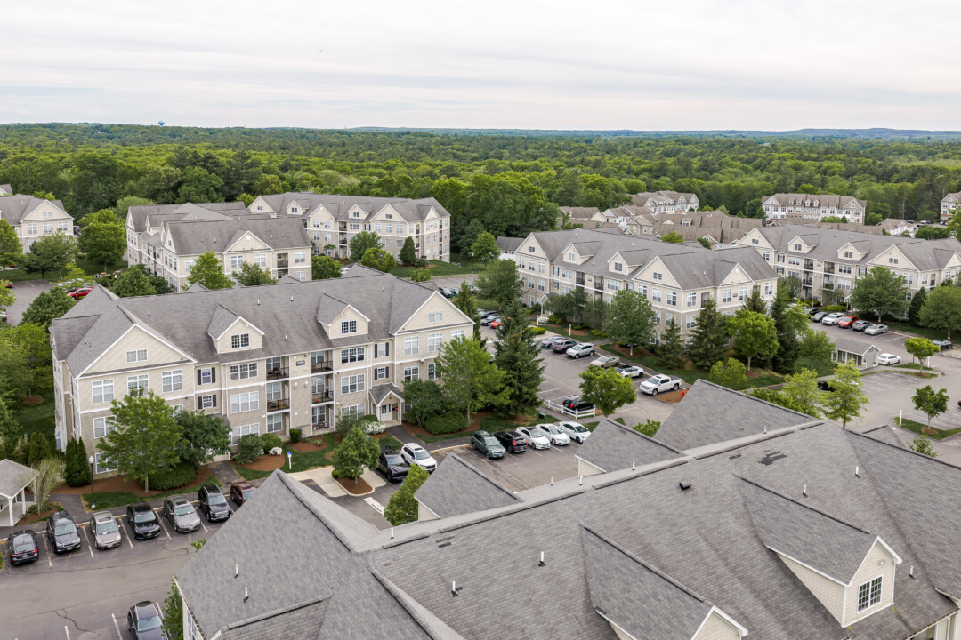 Aerial view of apartment buildings, parking areas, landscaped grounds, and surrounding trees.