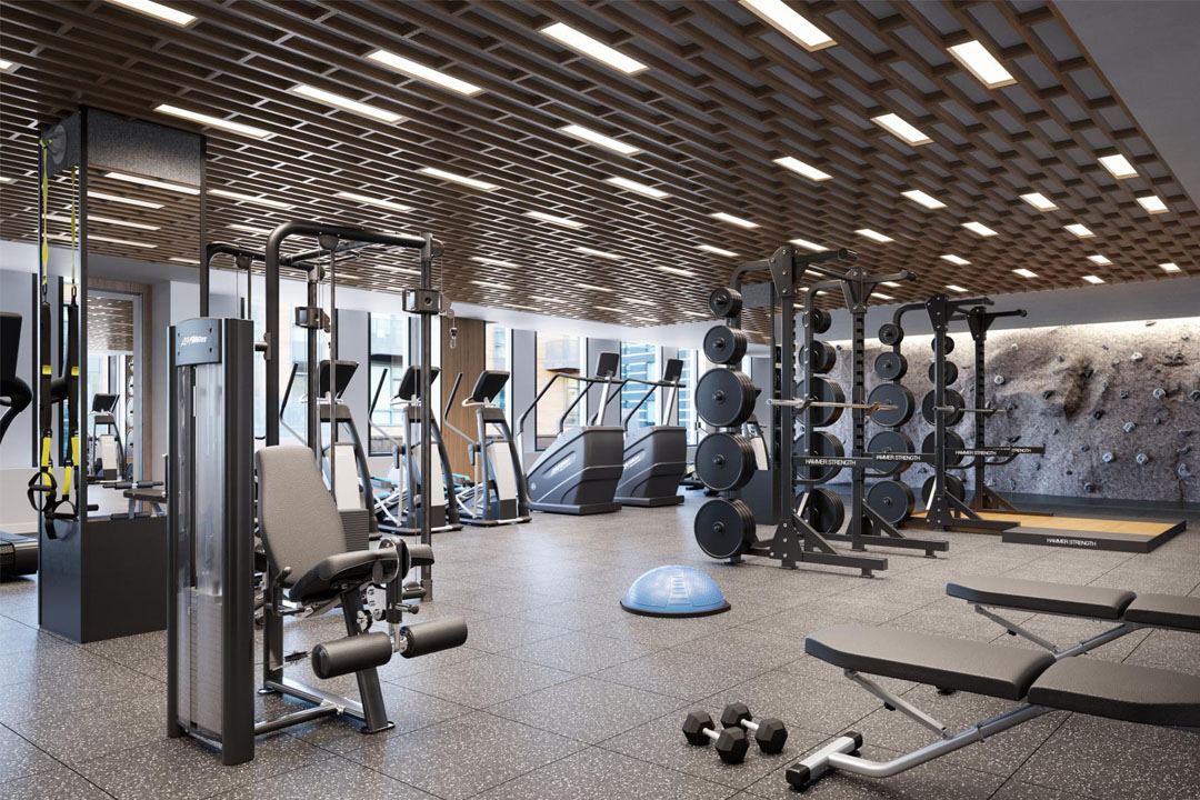 Large fitness room with many cardio and weight machines, weights, bouldering wall, and large windows.