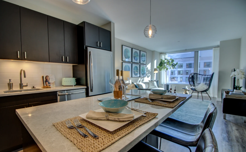 Open floor plan kitchen with high ceilings, brown wood cabinets, island, dishwasher, and refrigerator leading to living room