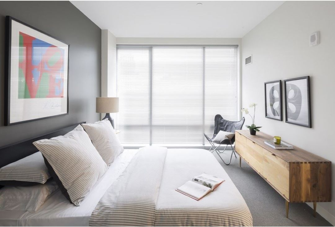 small grey and beige bedroom brightly lit with picture window