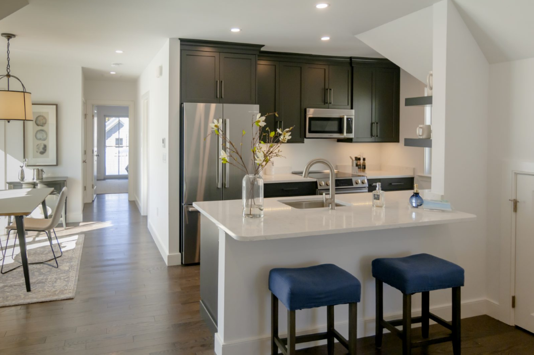 Open floor plan kitchen with black cabinets, white countertops, refrigerator, microwave, and flat-top stove/oven,