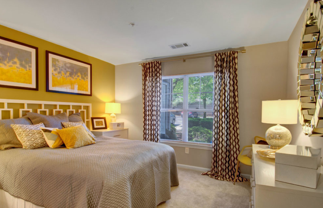 small beige bedroom with large window and carpeting