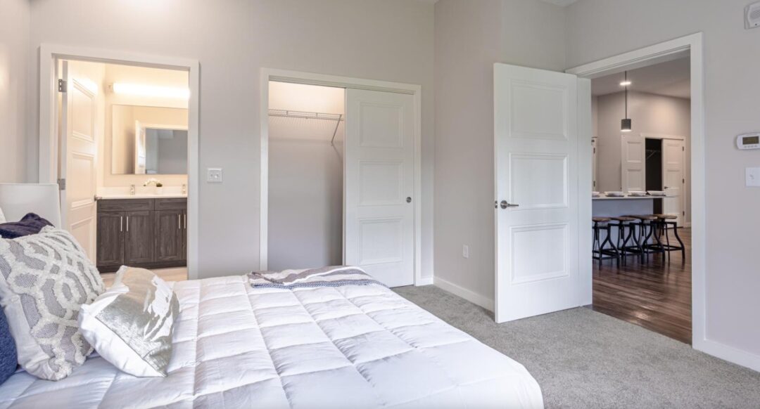 small bedroom with beige walls, and carpet floors. Bathroom attached and spacious closet