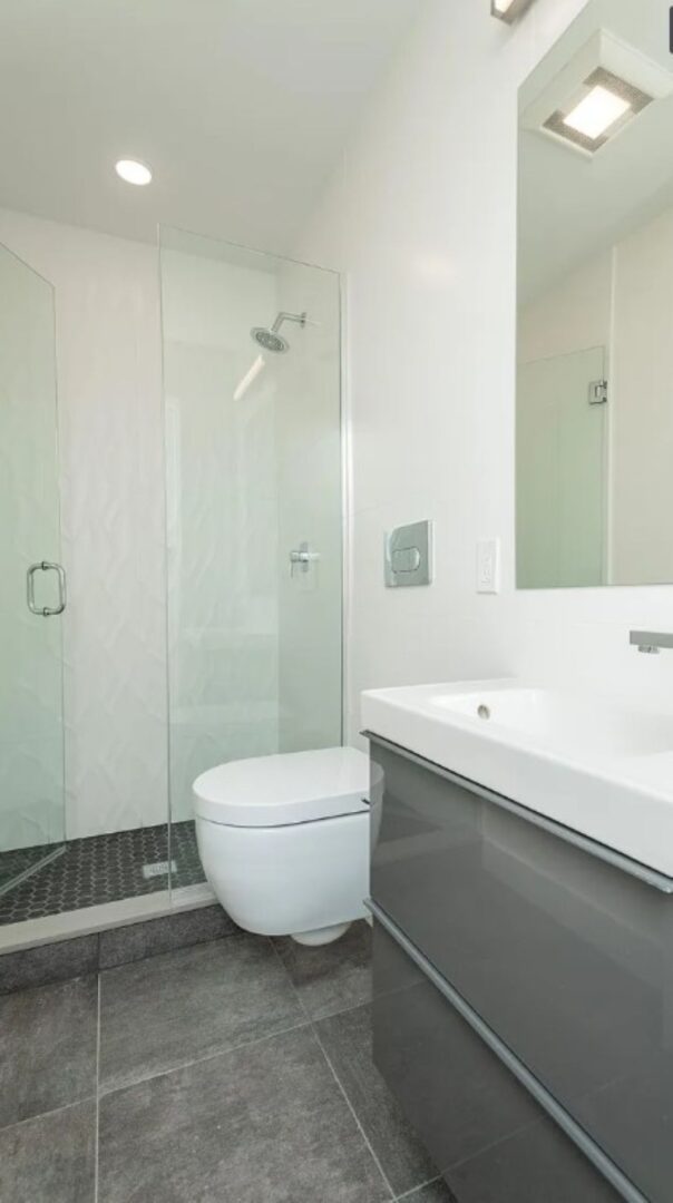 small bathoom with glass shower, grey tile and white accent features