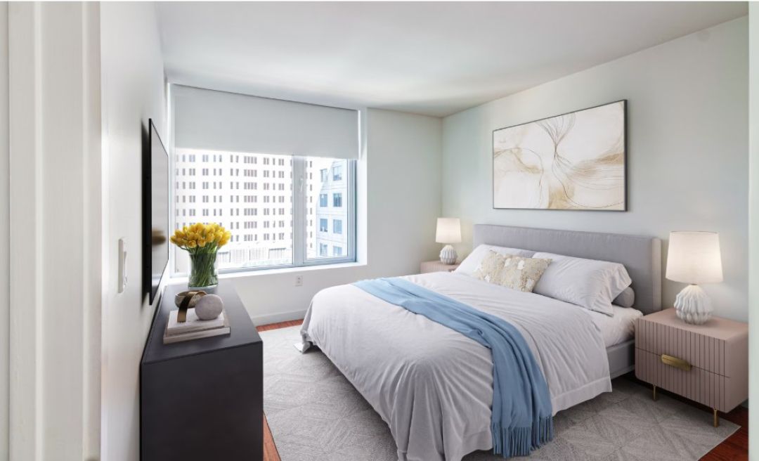 small beige bedroom with bed against wall, large picture window, and carpet floors