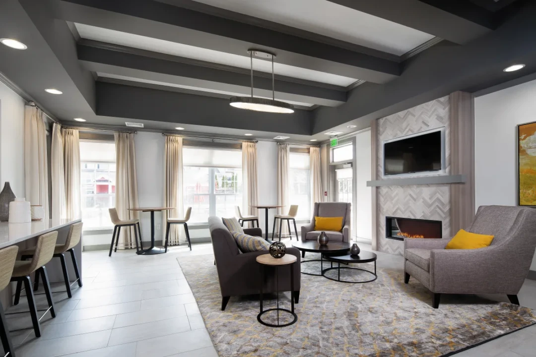 Resident lounge with gray seating, tables, a fireplace, and a wall-mounted television.