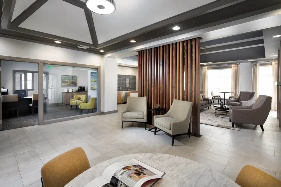 Bright lobby and leasing area with chairs, tables, and a wooden divider.