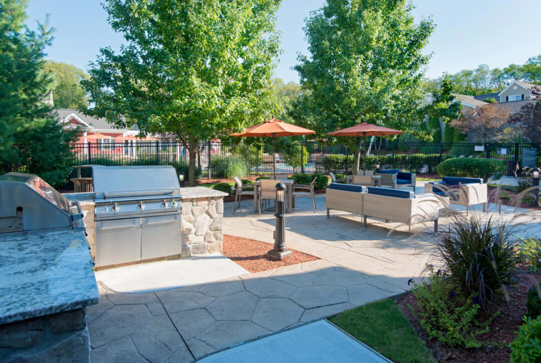 Outdoor patio with barbecue grills, tables, seating, umbrellas, and surrounding trees.