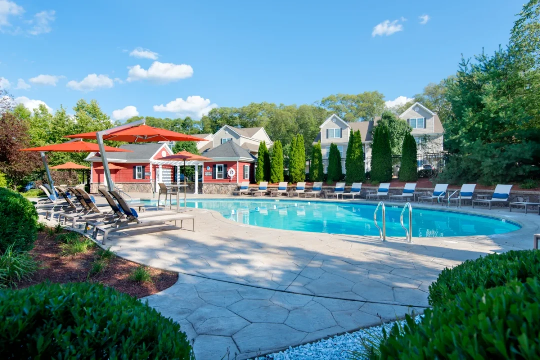 Outdoor swimming pool with lounge chairs, orange umbrellas, and landscaped greenery.