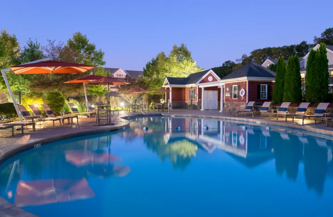 Outdoor swimming pool at dusk with lounge chairs, orange umbrellas, and surrounding lights.