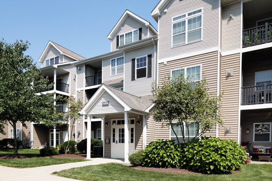 The modern exterior of a 3-story apartment complex featuring beige siding and white trim with landscaped entrance