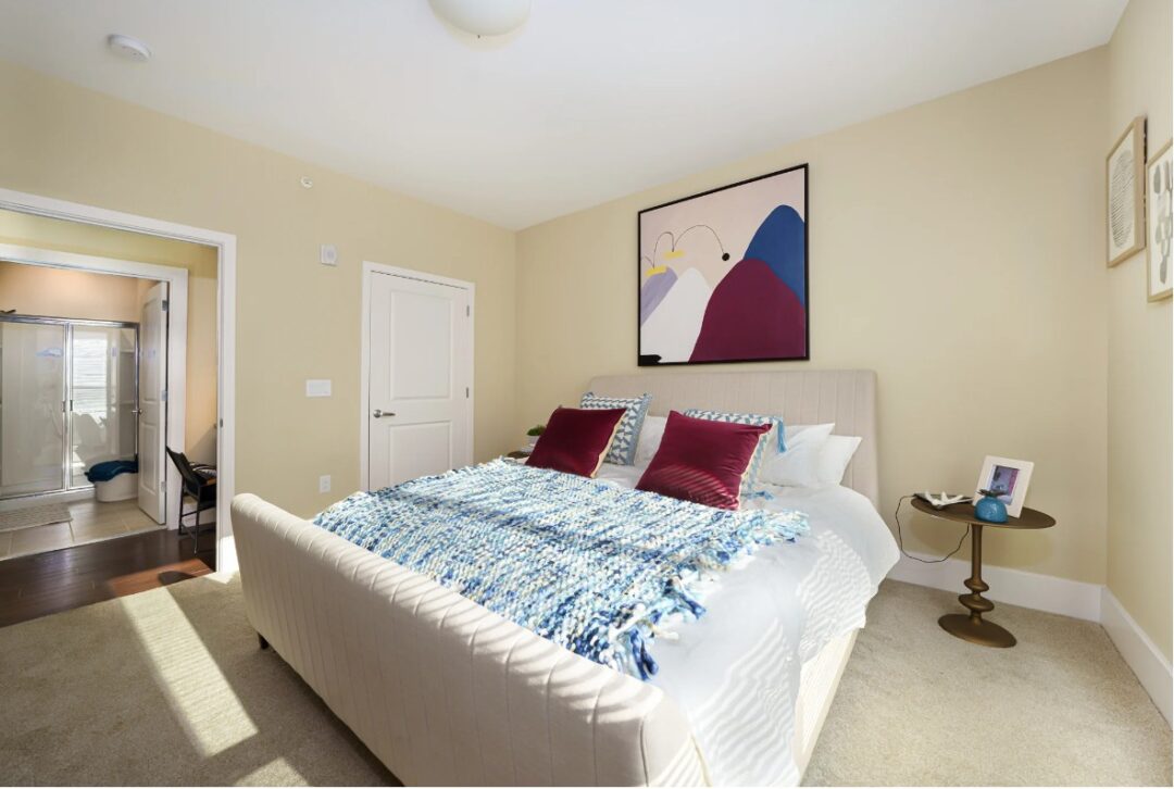 small beige bedroom with carpet and bed in the center