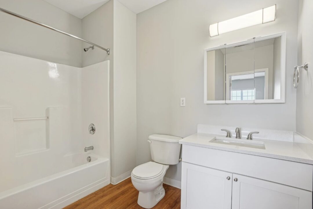 A simple apartment bathroom with a toilet, a white vanity with sink, and a shower/tub