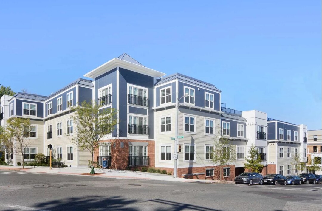 3 story apartment style building with blue and white siding and brick facade