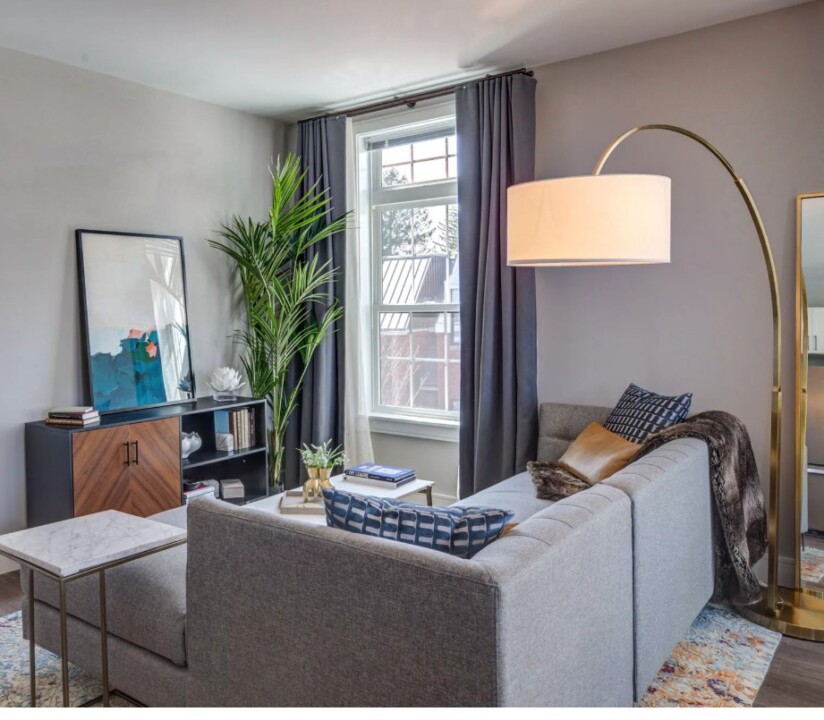 A bright, open-concept living room featuring wide-plank wood-style flooring and large floor-to-ceiling windows that provide ample natural light