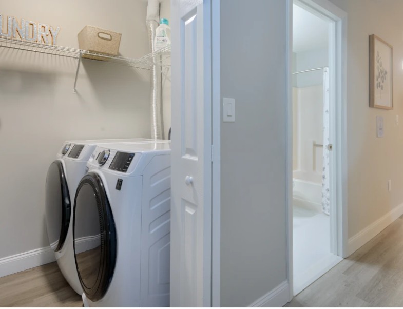side by side washer and dryer in closet with doors and storage shelf