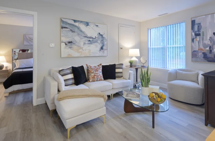 updated living room with white couch and table in center with wood floors and natural light