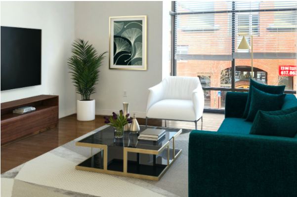 Living room with white walls, featuring a teal sofa, white padded chair, and a square glass coffee table with decorative items on a light area rug. A wooden media console with a mounted TV, a potted plant, and framed wall art sits beside a large window.