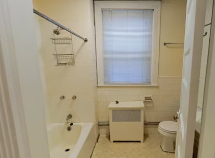 Bathroom with a bathtub and shower, white vanity, window, towel bars, and light-colored walls.