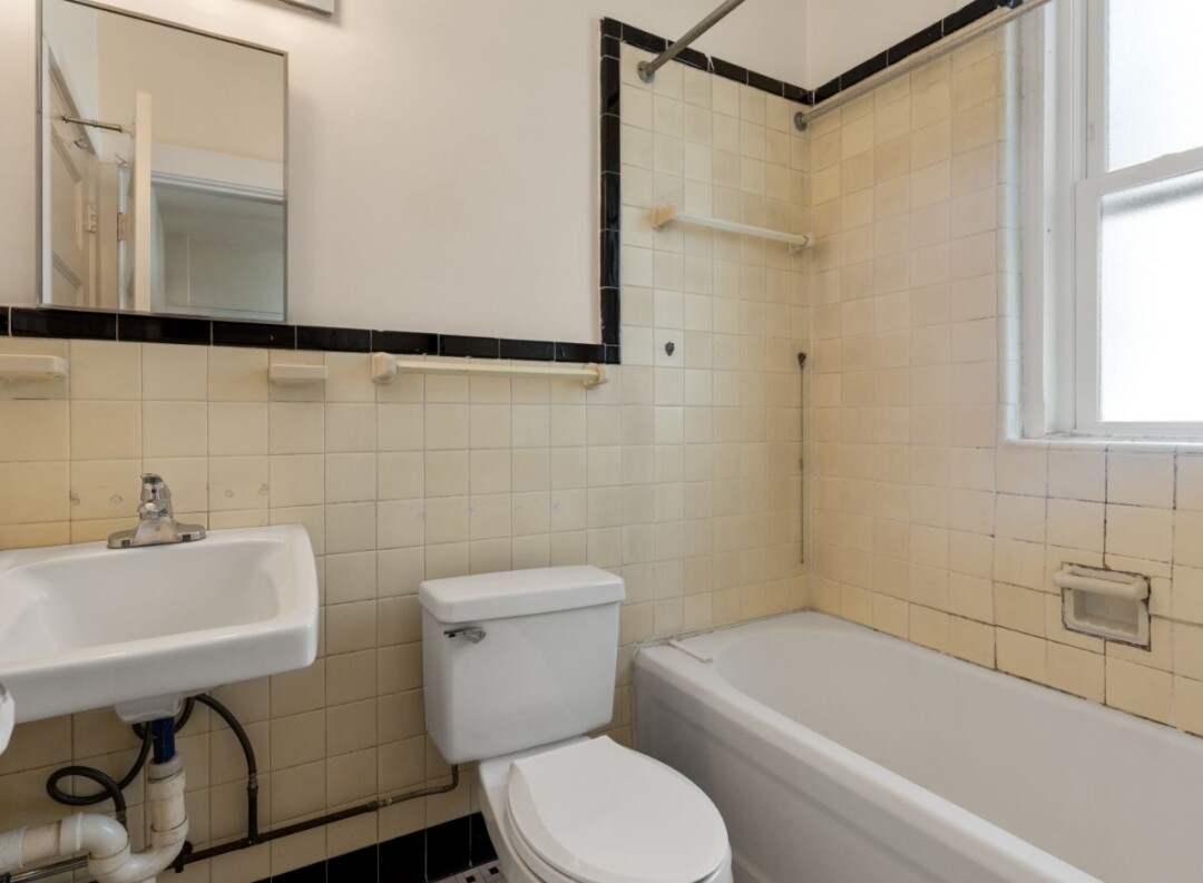 Bathroom with a shower, toilet, pedestal sink, window, and light colored walls.