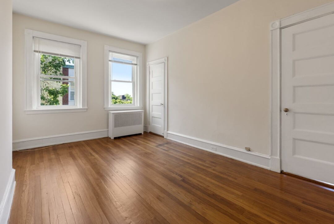 Bedroom with white walls, hardwood flooring, two windows, and a closet with a white door.