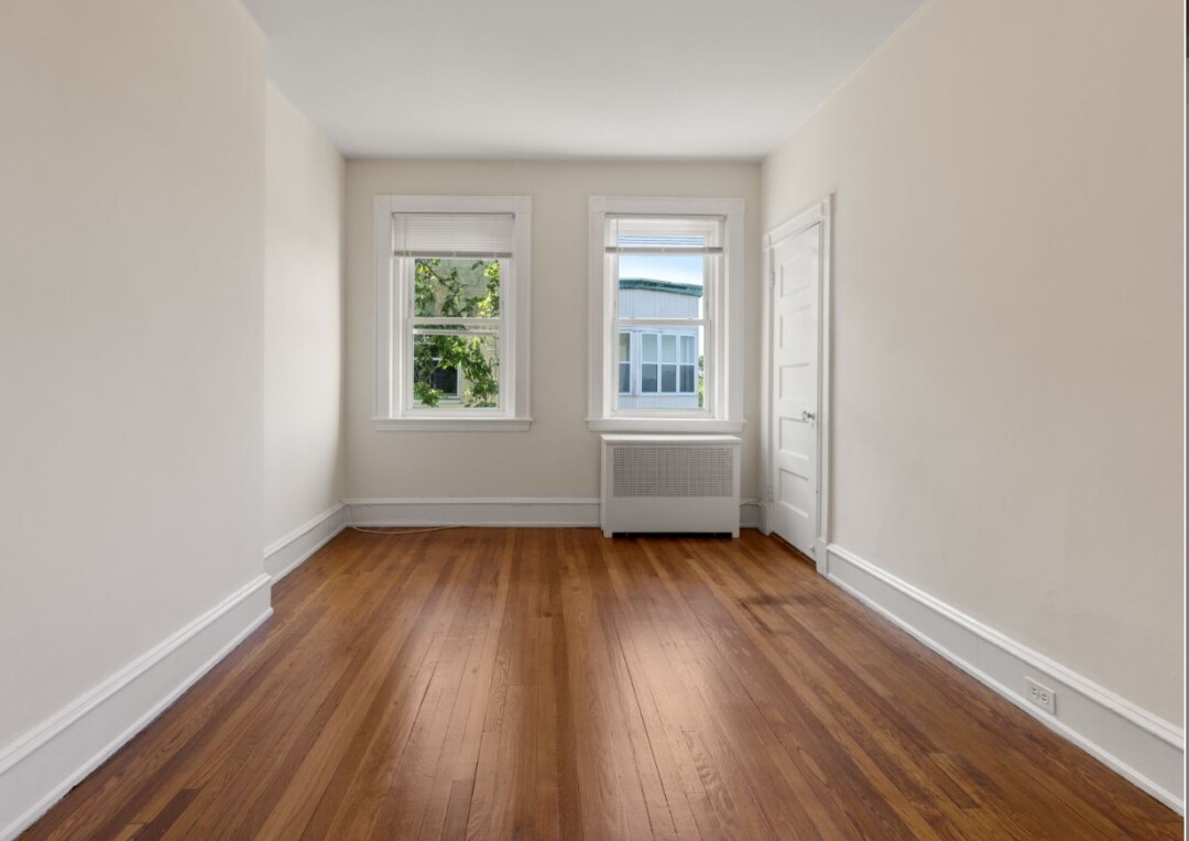 Bedroom with white walls, hardwood flooring, two windows, and a closet with a white door.