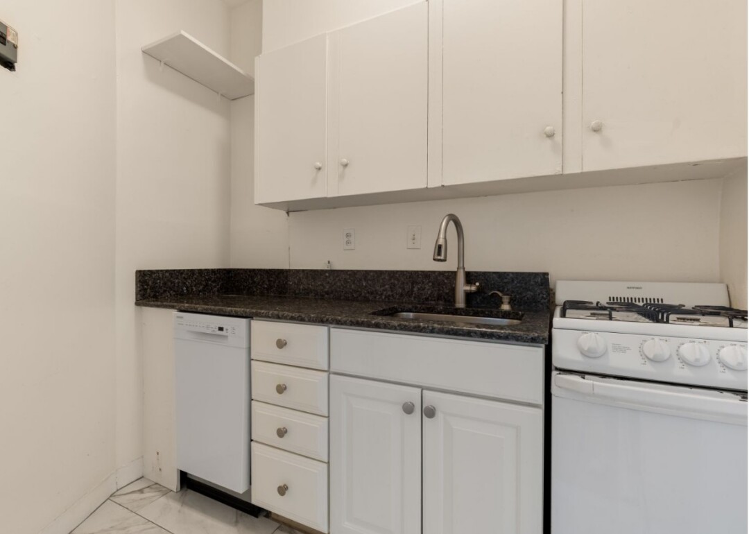 Kitchen with white cabinets, dark countertop, stainless steel sink, gas range, and white flooring.
