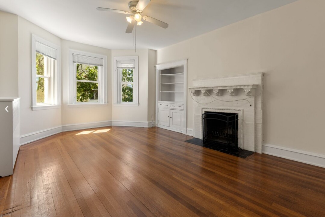 Living room with hardwood floors, white walls, ceiling fan, bay windows, and built-in shelving.