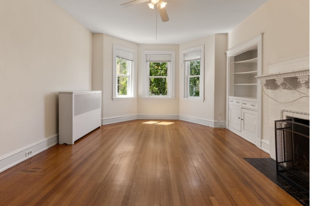 Living room with hardwood floors, white walls, ceiling fan, fireplace, and built-in shelving.