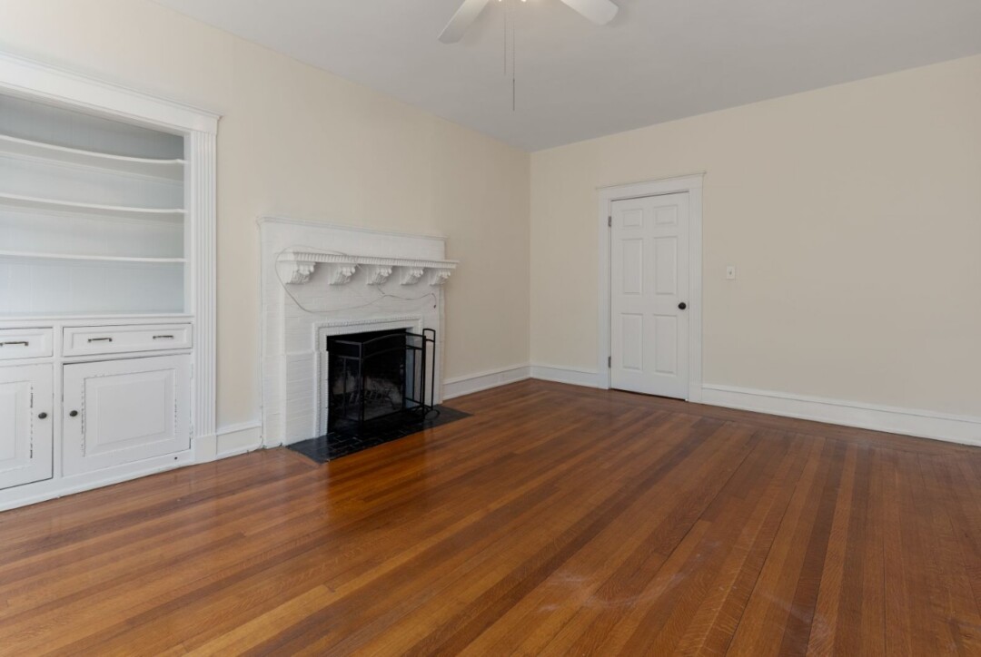 Living room with hardwood floors, white walls, decorative fireplace, ceiling fan, and built-in shelving.