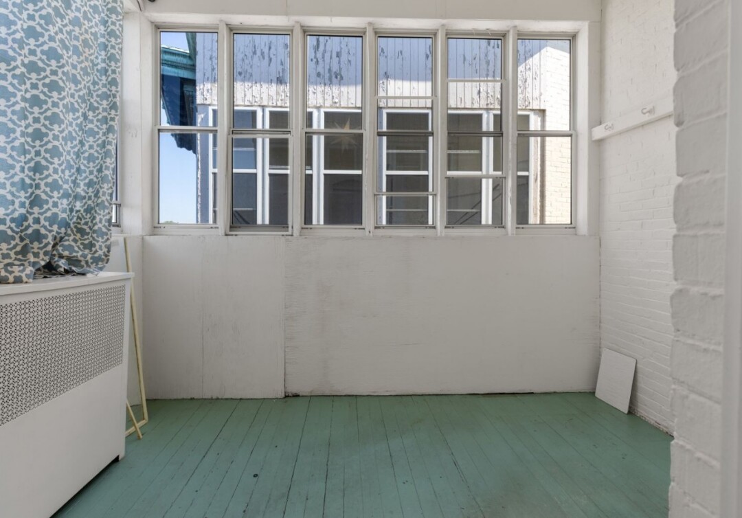 Bright porch with white painted brick walls, large windows, and painted light green flooring.