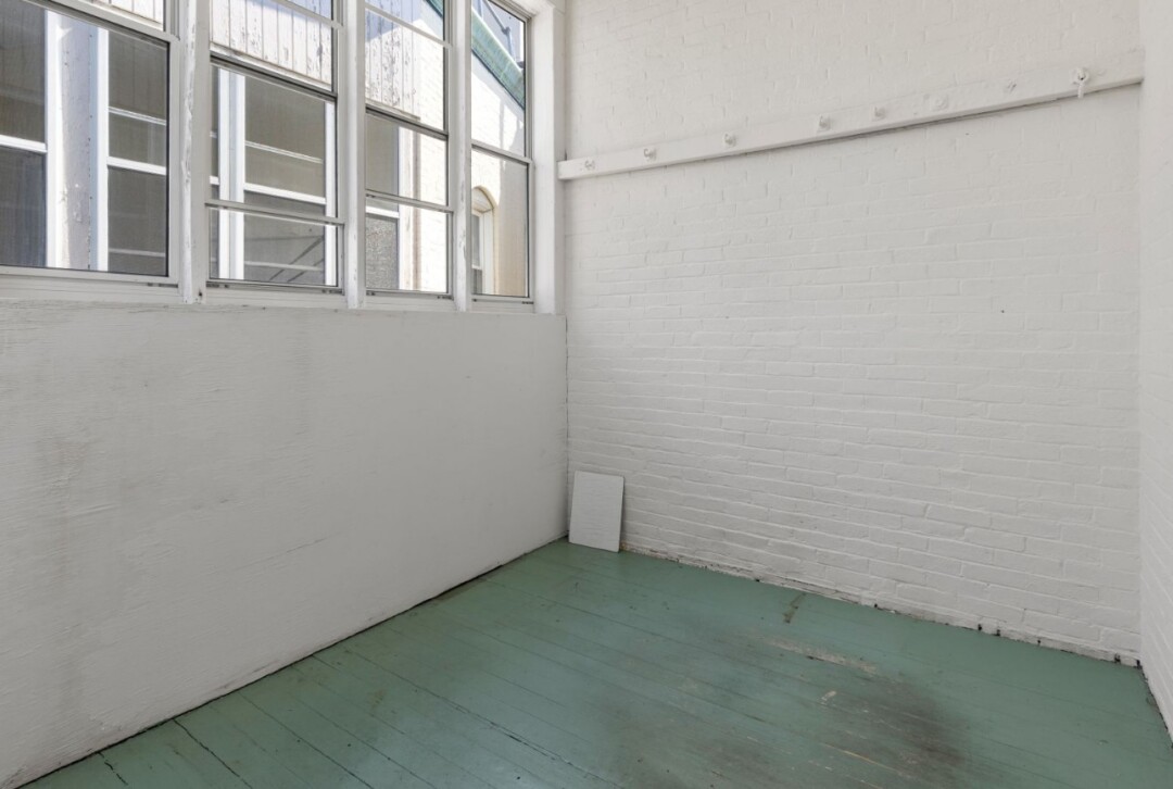Enclosed porch with white walls, multiple windows, and painted light green flooring.