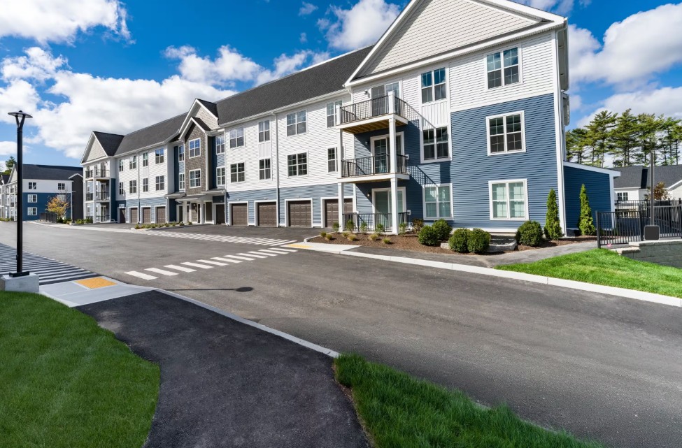 Exterior of a modern, multi-story apartment building with blue-and-white siding and an adjacent parking lot.