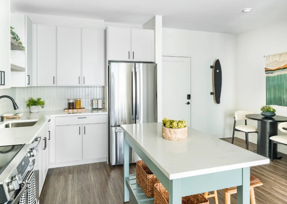 Bright white kitchen with stainless-steel appliances, pale blue island, and woven storage baskets.