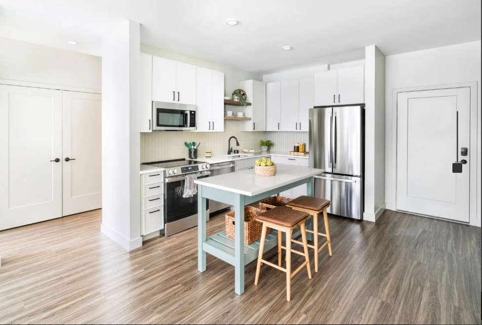 Open-concept kitchen with white cabinets, stainless-steel appliances, a blue island, and wooden stools.
